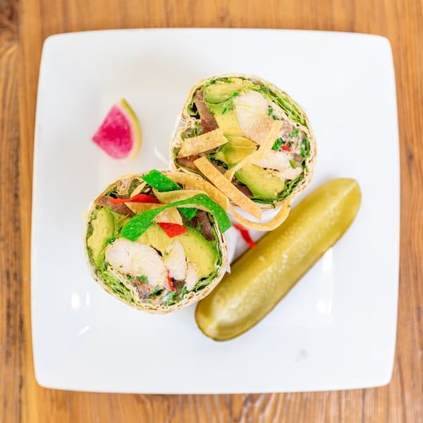 Two halves of a chicken and avocado wrap with tortilla strips, served with a pickle and watermelon radish.