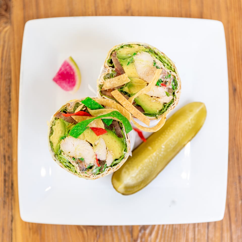 Two halves of a chicken and avocado wrap with tortilla strips, served with a pickle and watermelon radish.