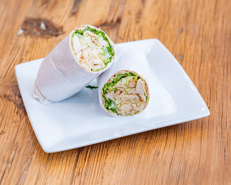 Two chicken and lettuce wraps, cut in half, on a white rectangular plate on a wooden table.
