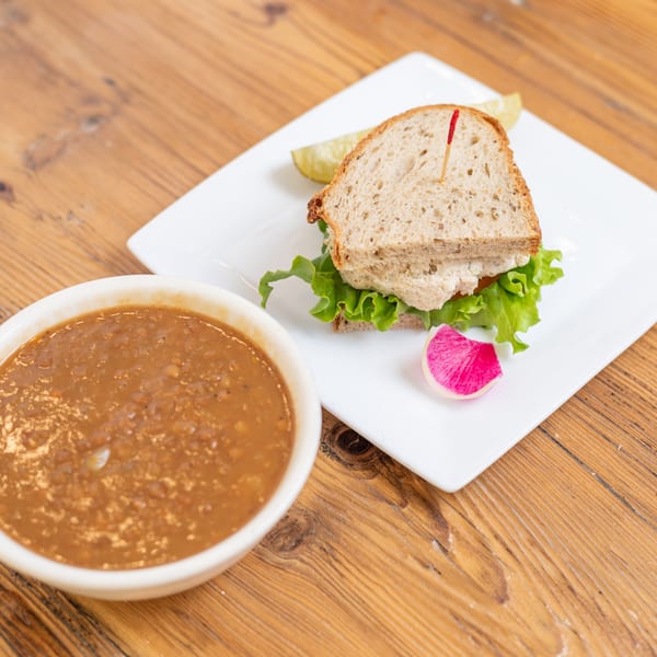 Bowl of lentil soup and a salad sandwich with lettuce, pickle, and radish on a wooden table.