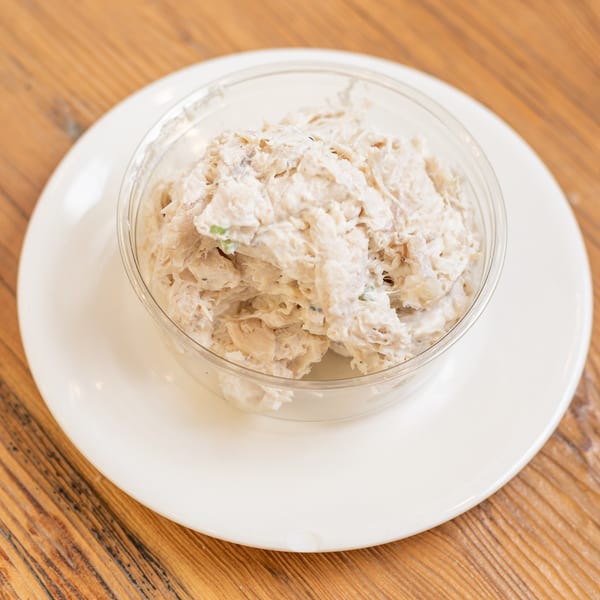 Creamy chicken salad in a clear bowl on a white plate and wooden table.
