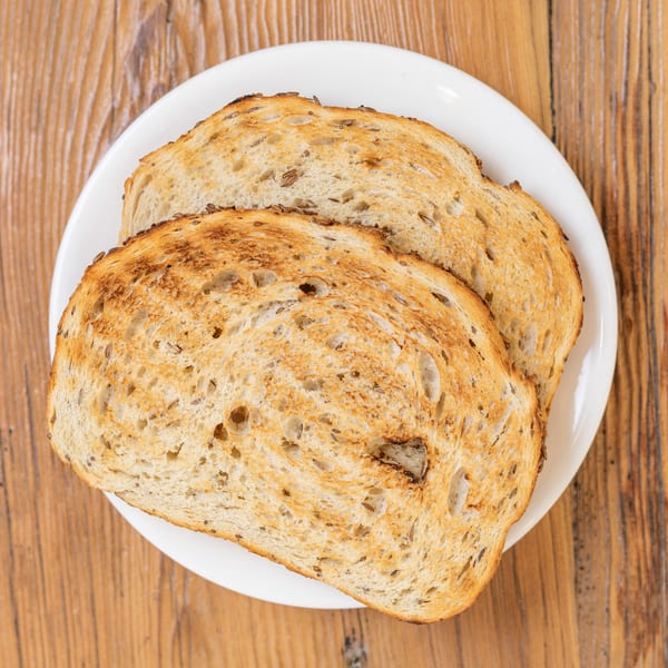 Two slices of golden brown seeded toast on a white plate, on a wooden table.