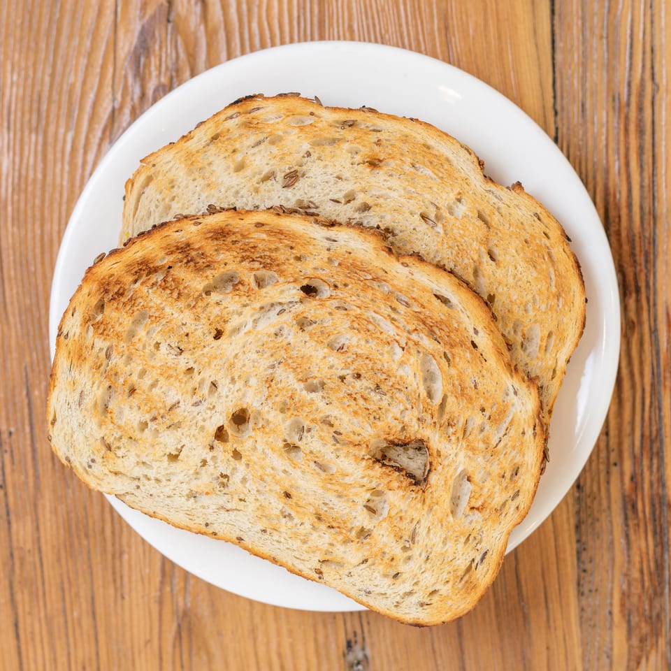 Two slices of golden brown seeded toast on a white plate, on a wooden table.
