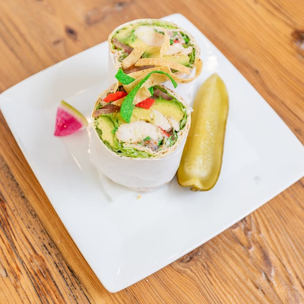 Chicken and avocado wrap halves with tortilla strips, served with a pickle and watermelon radish on a white plate.