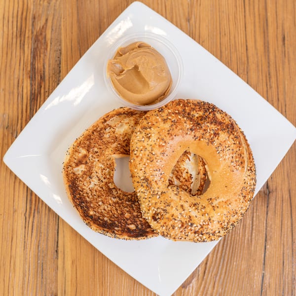 Two toasted bagel halves, one everything, with a side of peanut butter on a white plate.