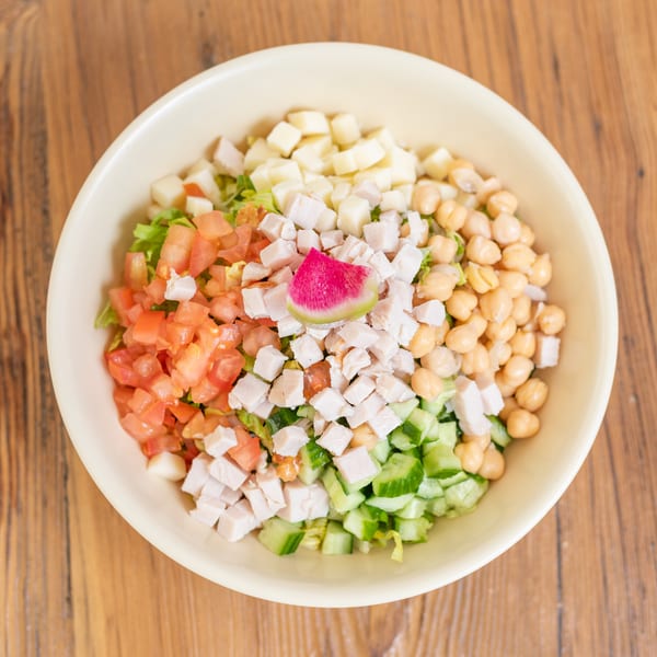 Fresh chopped salad with chicken, tomatoes, chickpeas, cheese, cucumbers, and a watermelon radish slice.