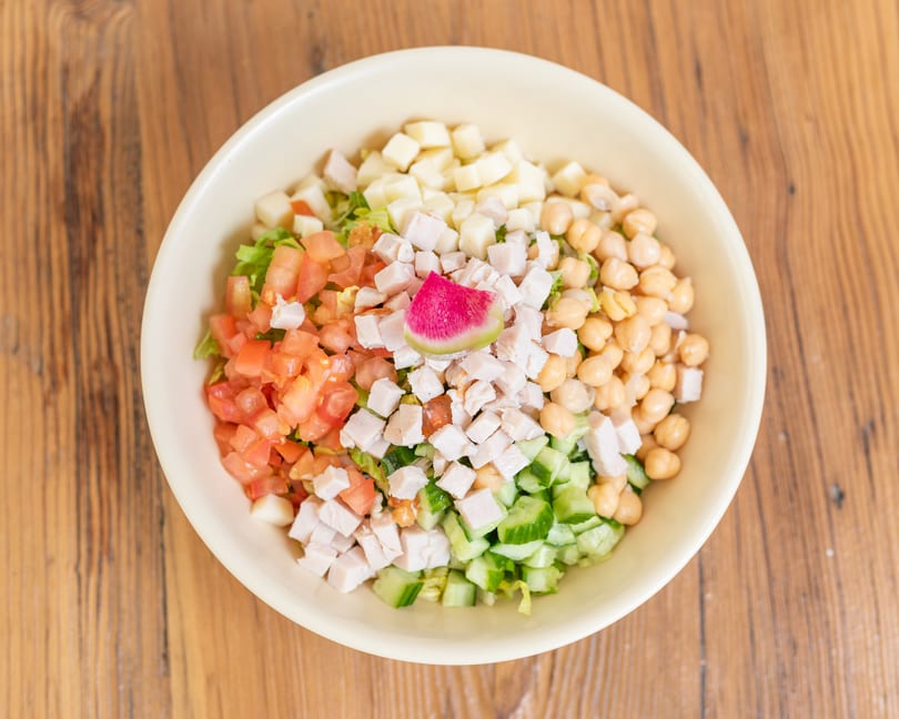 Fresh chopped salad with chicken, tomatoes, chickpeas, cheese, cucumbers, and a watermelon radish slice.