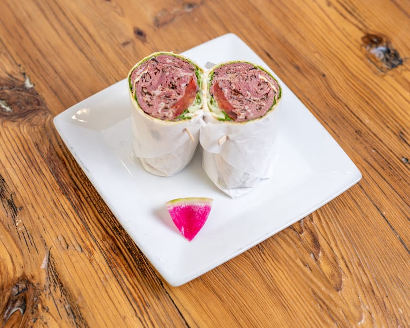 Deli meat wrap cut in half on a white plate, served with a pink watermelon radish.