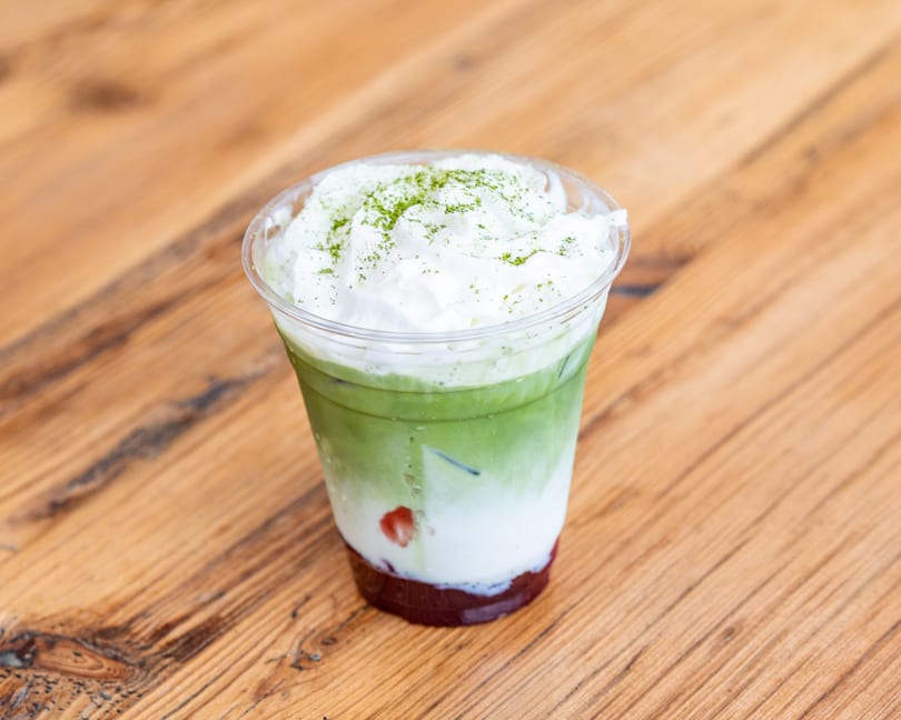 Iced matcha latte with whipped cream and strawberry puree on a wooden table.