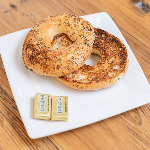 Toasted everything bagel halves on a white plate with two pats of Grassland butter on a wooden table.