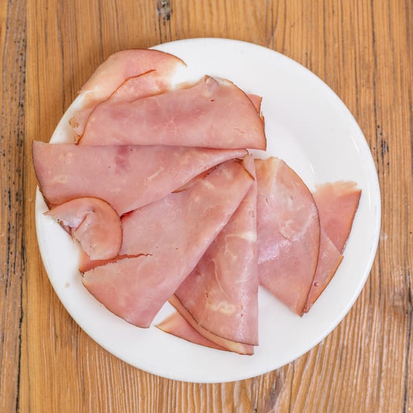 A white plate filled with folded slices of pink deli ham on a wooden table.