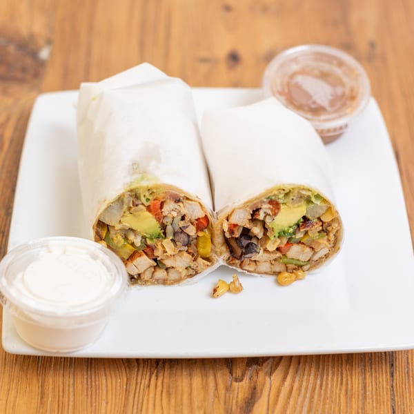Two chicken and avocado burritos, cut in half, served on a white plate with two dipping sauces.