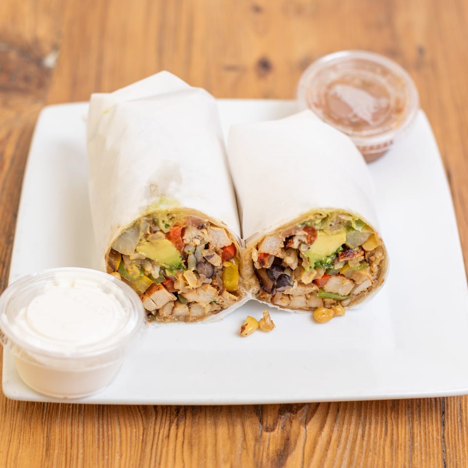Two chicken and avocado burritos, cut in half, served on a white plate with two dipping sauces.