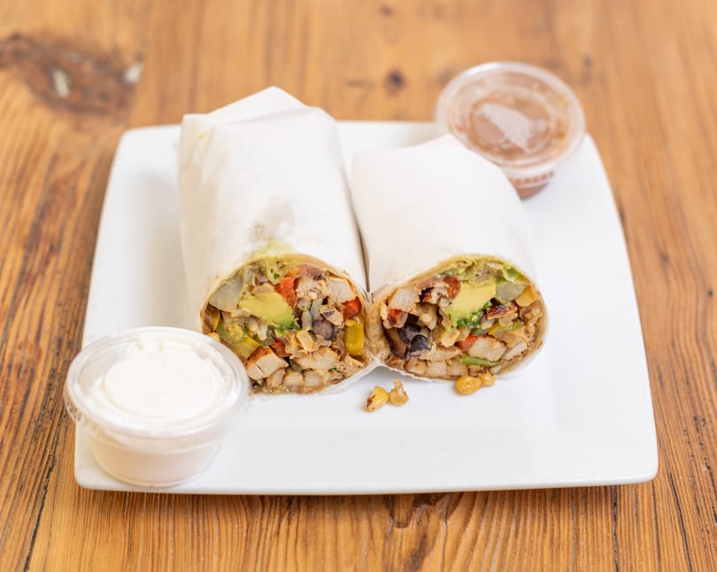 Two chicken and avocado burritos, cut in half, served on a white plate with two dipping sauces.