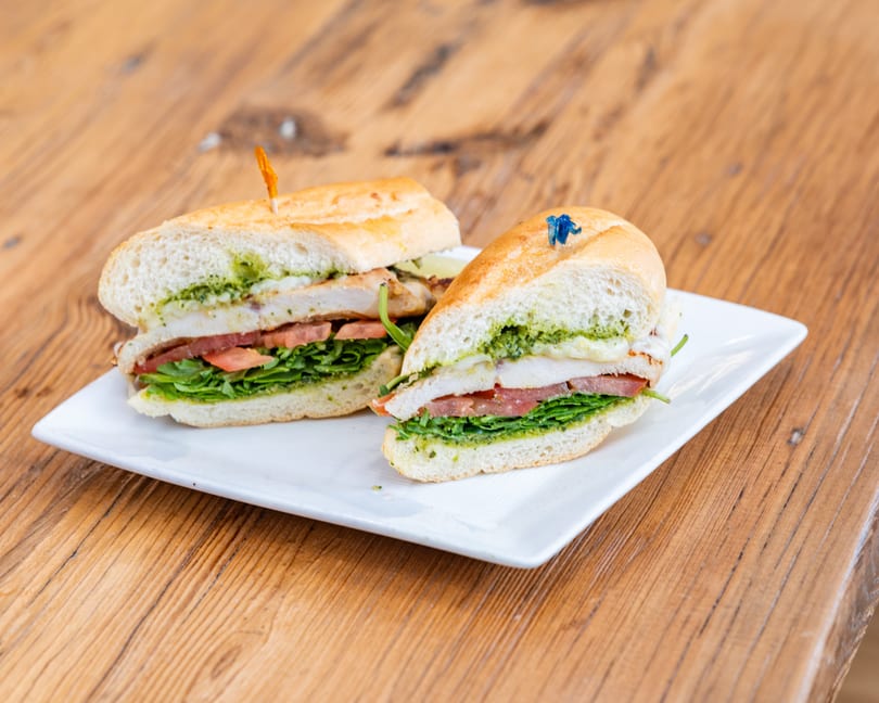 Two halves of a chicken pesto sandwich with lettuce and tomato on a white plate.
