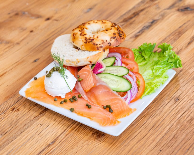A bagel with lox, cream cheese, capers, dill, lettuce, tomatoes, cucumbers, and red onions.