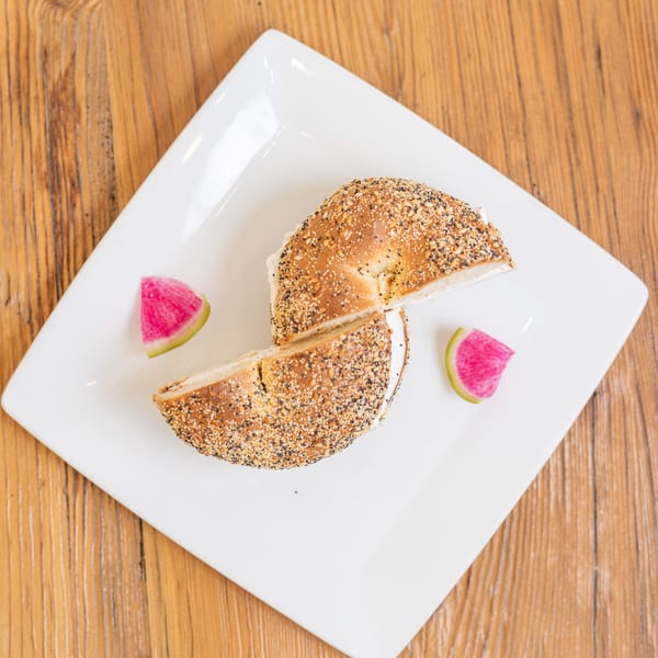 Cream cheese everything bagel, cut in half, served with watermelon radish on a white plate.