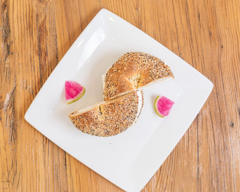 Cream cheese everything bagel, cut in half, served with watermelon radish on a white plate.