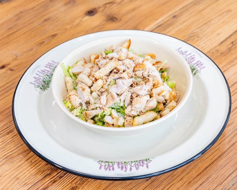 Chicken Caesar salad with croutons and parmesan cheese in a white bowl on a wooden table.
