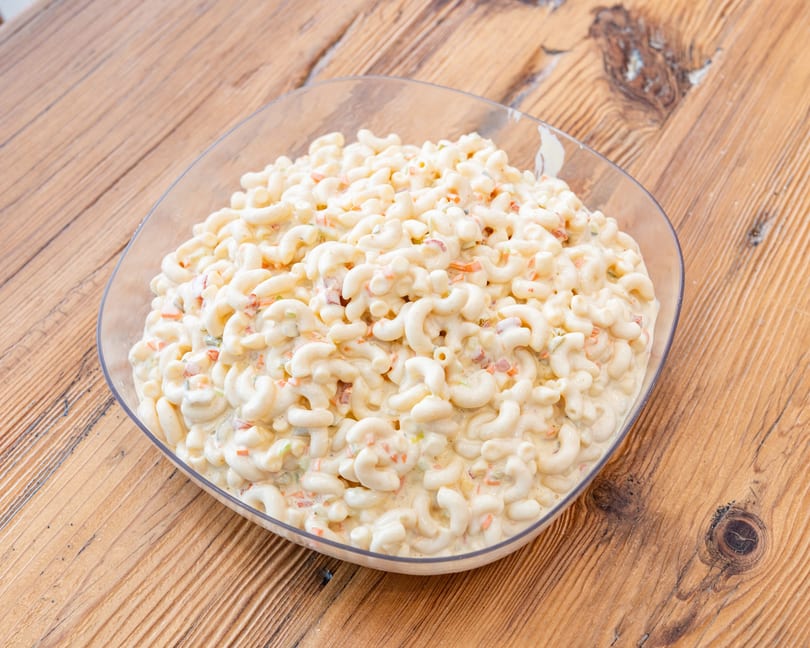 A large clear bowl of creamy macaroni salad with diced vegetables on a wooden table.