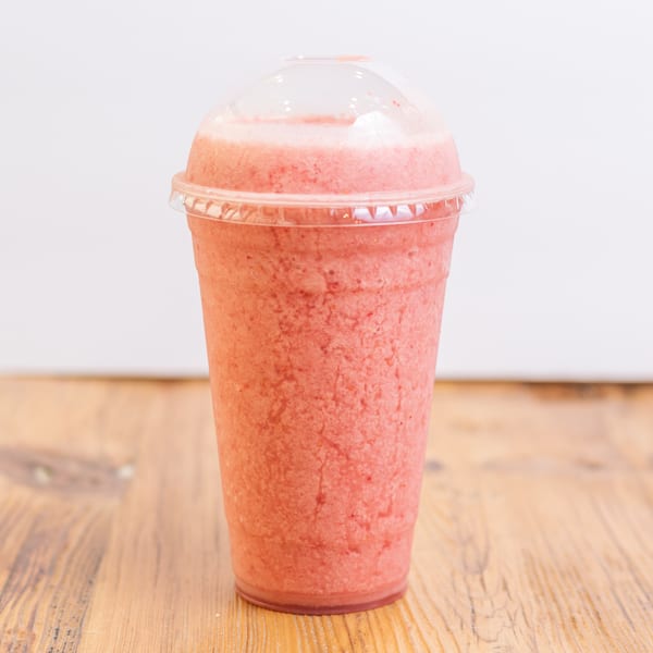 Pink smoothie in a clear plastic cup with a dome lid on a wooden table.