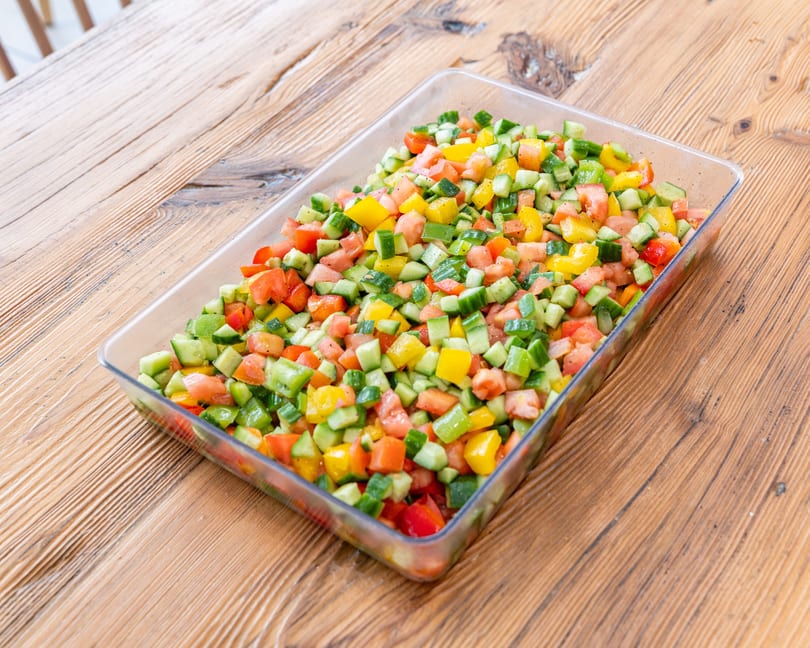 A clear rectangular dish filled with a colorful salad of diced cucumbers, tomatoes, and bell peppers.