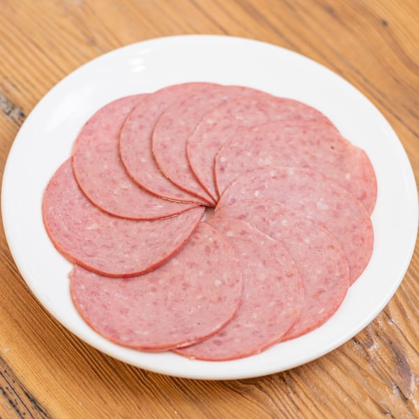 Sliced salami arranged in a circle on a white plate, on a wooden table.